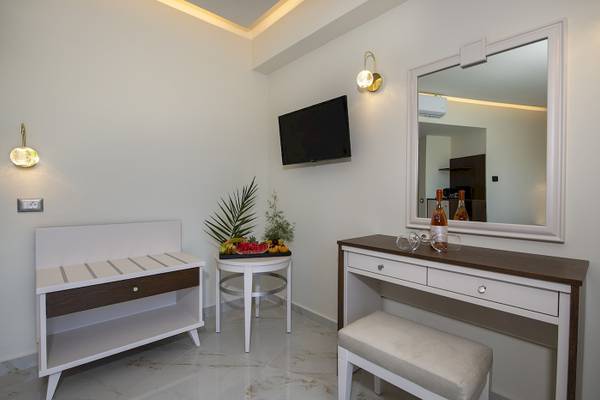Innenansicht eines eleganten Zimmers im Vantaris Luxury Beach Resort mit einem Fernseher an der Wand, einem kleinen Tisch mit Obst und einem großen Spiegel.