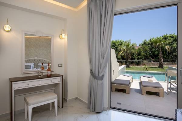 Innenansicht eines Zimmers im Vantaris Luxury Beach Resort mit Blick auf einen Swimmingpool und Liegen.