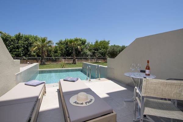Pool-Terrasse im Vantaris Luxury Beach Resort mit Sonnenliegen, einem Tisch und einem Pool im Hintergrund.