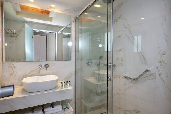 Das Badezimmer des Vantaris Luxury Beach Resort mit Marmorwänden, einer Badewanne und einer Dusche.