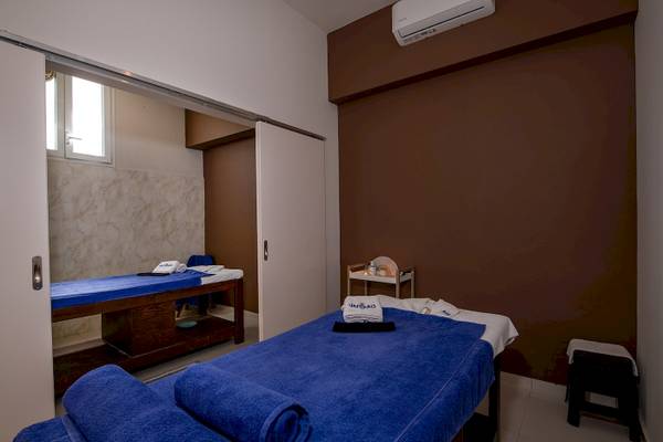 Massageraum im Vantaris Luxury Beach Resort mit zwei Massagebetten, blauen Handtüchern und einem Tisch.