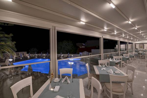 Nachtansicht des Poolrestaurants im Vantaris Luxury Beach Resort mit blau beleuchtetem Pool und gedeckten Tischen.