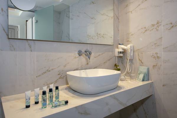 Badezimmer des Vantaris Luxury Beach Resort mit Marmorwänden, einem Waschbecken und Pflegeprodukten.