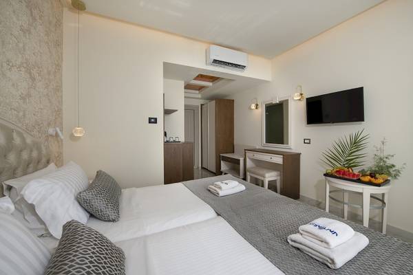 Schlafzimmer im Vantaris Luxury Beach Resort mit zwei Betten, grauen Decken, weißen Kissen und Obst auf einem Tisch.