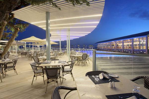 Außenbereich des Arina Beach Resorts mit Tischen und Stühlen unter großen Sonnenschirmen.