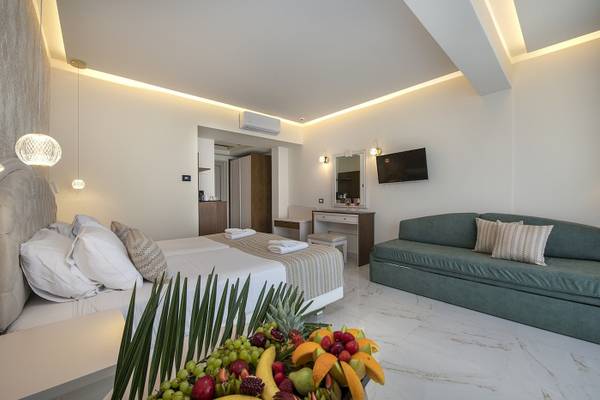 Innenansicht eines eleganten Schlafzimmers im Vantaris Luxury Beach Resort mit einem Doppelbett, einem Schlafsofa, einer Obstschale und modernen Einrichtungen.