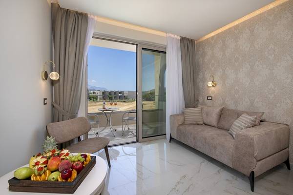 Innenansicht einer Suite im Vantaris Luxury Beach Resort mit Balkon, Tisch, Stühlen, Früchten und Sofa.