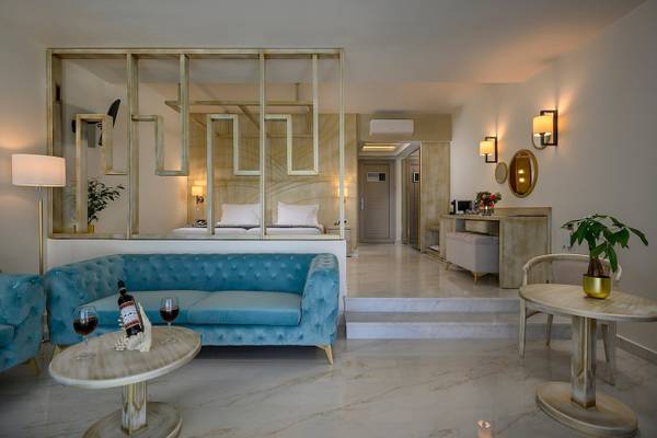 Innenansicht des Schlafzimmers im Vantaris Palace Hotel mit einem blauen Sofa, zwei Weingläsern und einer Flasche Wein auf einem Tisch.