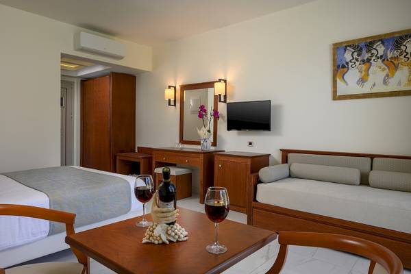 Innenansicht eines Zimmers im Vantaris Palace Hotel mit Bett, Tisch, Wein und Dekor.