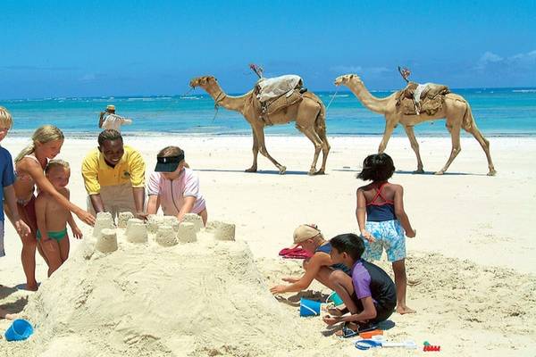 Kinder bauen einen Sandburg am Strand des Southern Palms Beach Resorts mit Kamelen im Hintergrund.