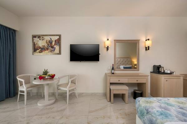 Inneneinrichtung eines Zimmers im Vantaris Palace Hotel mit Tisch, Stühlen, Fernseher, Spiegel und Nachttisch.