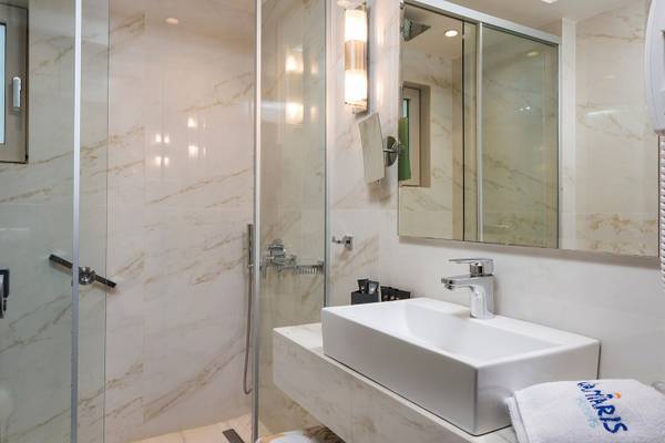 Badezimmer im Vantaris Palace Hotel mit Marmorwänden, Glasdusche und Waschbecken.