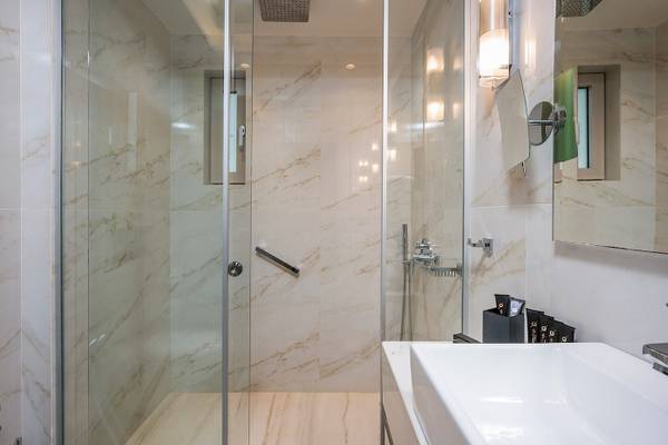 Badezimmer im Vantaris Palace Hotel mit Marmorwänden, Glasdusche und Waschbecken.