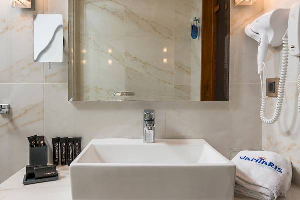 Badezimmer im Vantaris Palace Hotel mit Waschbecken, Spiegel und Handtuchtrockner.