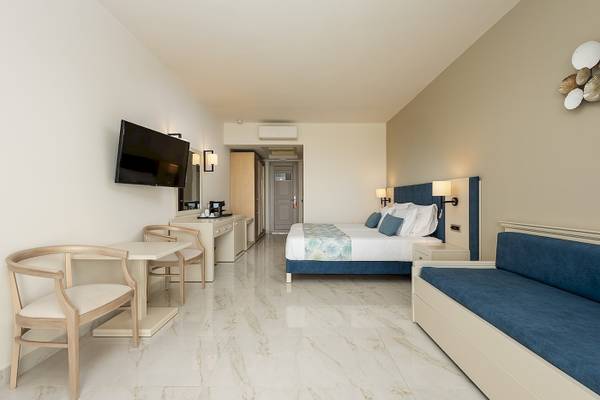 Innenansicht eines Hotelzimmers im Vantaris Palace mit Fernseher, Schreibtisch, Sessel und Bett.
