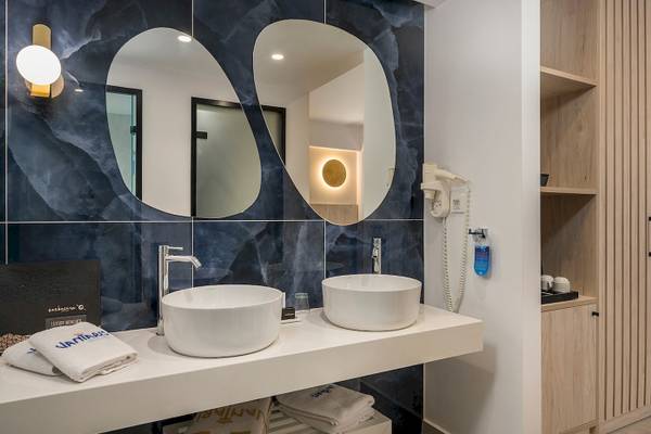 Badezimmer im Vantaris Palace mit zwei Waschbecken, Spiegeln und blauer Wandgestaltung.