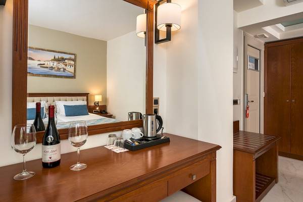 Zimmer im Vantaris Palace Hotel mit Bett, Weinflasche und Gläsern auf einem Schreibtisch.