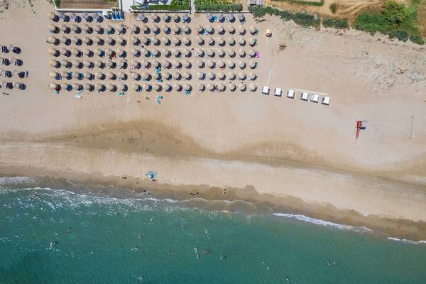 Luftaufnahme des Vantaris Palace Strandes mit vielen Sonnenschirmen und Menschen im Wasser.