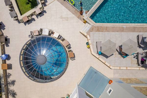 Luftaufnahme des Swimmingpool-Bereichs des Vantaris Palace Hotels mit Sonnenliegen und Sonnenschirmen.
