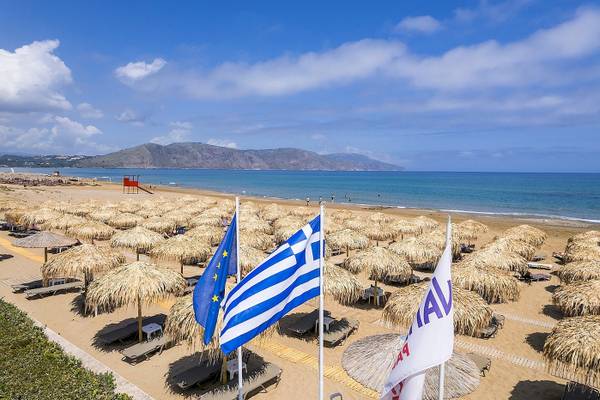 Strand des Vantaris Palace Hotels mit vielen Sonnenhuten und Liegen, Flaggen im Vordergrund