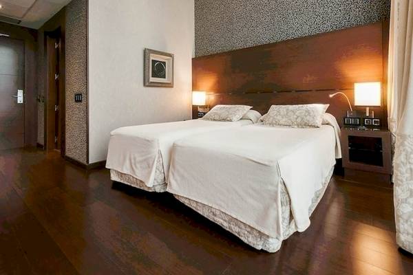 Schlafzimmer im Colonial Barcelona Hotel mit zwei Betten, Nachttischen und Lampen.