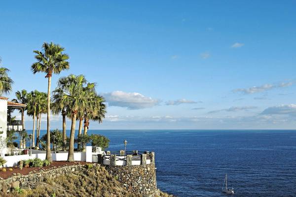 Aussicht des Jardin Tecina Hotels auf das Meer mit Palmen und einem Segelboot im Hintergrund.