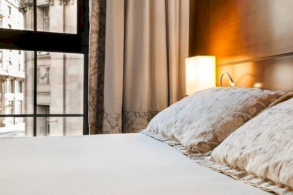 Bett im Colonial Barcelona Hotel mit Kissen und Fenster mit Stadtblick