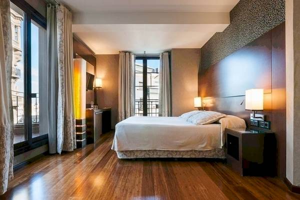 Innenansicht eines Zimmers im Colonial Barcelona Hotel mit Holzboden und heller Einrichtung.