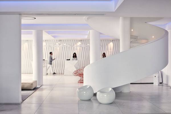 Lobby des Myconian Ambassador Relais & Chateaux Hotels mit Marmorboden und geschwungener Treppe.