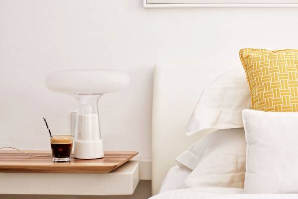 Hotelzimmer des Myconian Ambassador Relais & Chateaux mit Bett, gelbem Kissen und Nachttisch mit Lampe und Getränk.