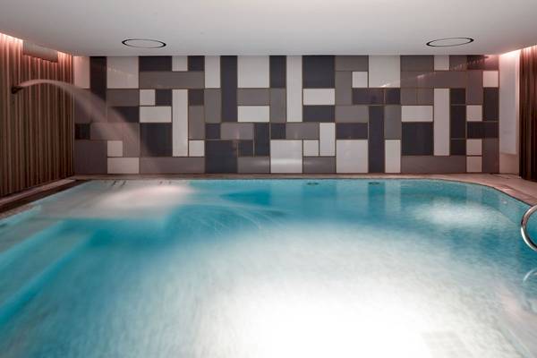 Schwimmbecken im Myconian Ambassador Hotel mit quadratischen Kacheln und Wasserstrahl.