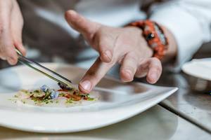 Koch in der Küche des Myconian Ambassador Relais & Chateaux, der ein Gericht auf einem Teller dekoriert