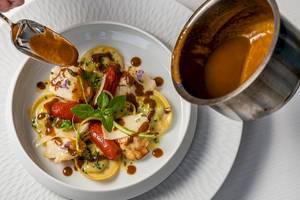 Ein Tellergericht mit gefüllten Teigtaschen, Tomaten, Basilikum und einer braunen Sauce.