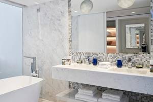 Luxuriöses Badezimmer im Myconian Ambassador Relais & Chateaux mit Badewanne, Doppelwaschbecken und Marmorfliesen.