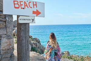 Frau steht am Strand vor einem Schild mit der Aufschrift Beach und einem Pfeil, der auf das Meer zeigt.