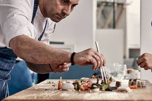 Koch im Myconian Ambassador Relais & Chateaux, der Sushi auf einem Holztisch zubereitet.
