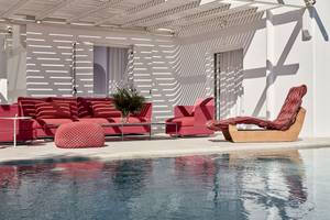 Poollounge im Myconian Ambassador Hotel mit roten Möbeln und einem weißen Gebäude.