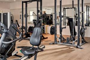 Fitnessstudio im Myconian Ambassador Relais & Chateaux mit verschiedenen Trainingsgeräten und Holzboden.