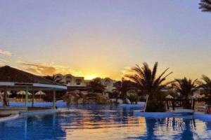 Pool im Djerba Holiday Beach Hotel bei Sonnenuntergang mit Palmen und Gebäuden im Hintergrund.