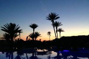 Palmen um einen Pool im Djerba Holiday Beach Hotel bei Sonnenuntergang.