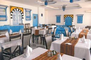 Innenansicht des Restaurants im Djerba Holiday Beach Hotel mit blauen und gelben Wandverzierungen und gepolsterten Stühlen.