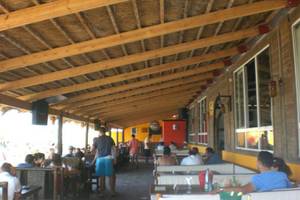 Innenansicht der Terrasse im Djerba Holiday Beach Hotel mit Gästen an Tischen und Holzbalkendecke.