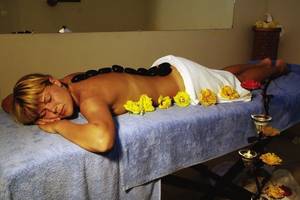 Eine Frau liegt mit geschlossenen Augen auf dem Rücken auf einem Massagetisch mit schwarzen Steinen und gelben Rosen im Hotel.