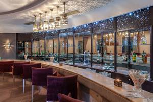 Innenansicht der Bar im Djerba Holiday Beach Hotel mit Bartheken, roten Stühlen und alkoholischen Getränken.