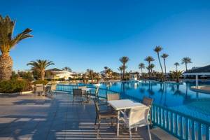 Außenpool des Djerba Holiday Beach Hotels mit umliegenden Tischen und Palmen