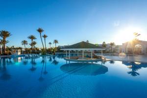 Außenpool des Djerba Holiday Beach Hotels mit Sonnenuntergang im Hintergrund.