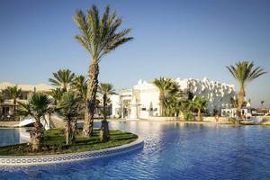 Außenansicht des Djerba Holiday Beach Hotels mit Pool, weißen Gebäuden und Palmen.