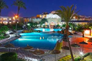 Abendliche Ansicht des Djerba Holiday Beach Hotels mit Swimmingpool und Palmen.