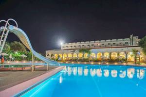 Nachtansicht des Swimmingpools im Irene Palace Beach Resort mit einer Wasserrutsche und beleuchtetem Gebäude.