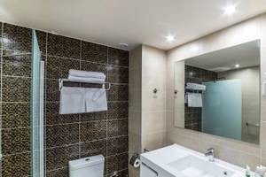 Badezimmer im Irene Palace Beach Resort mit gefliester Wand, Glasdusche und Spiegel.